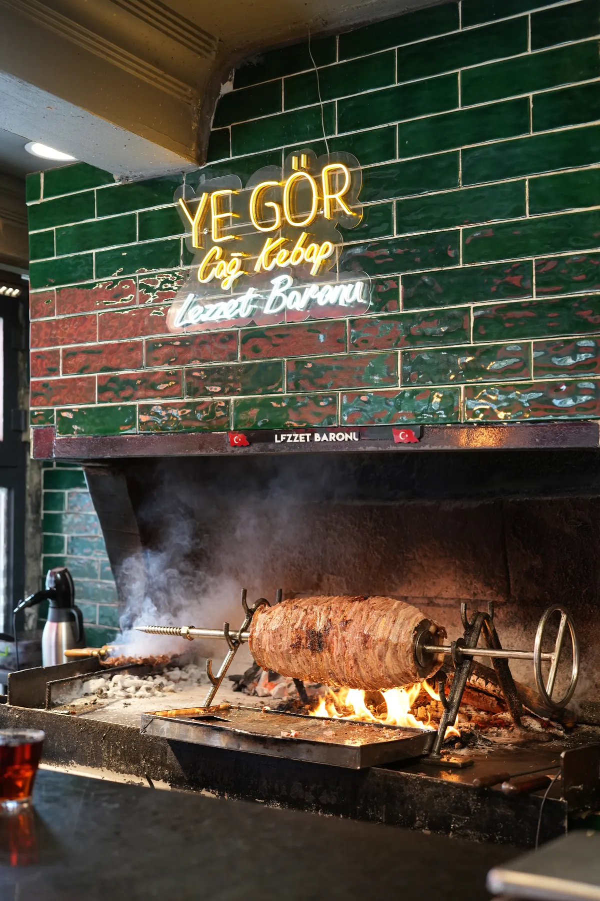 Ye Gör Cağ Kebap tabelası, yeşil seramik duvar ve yanan ocak